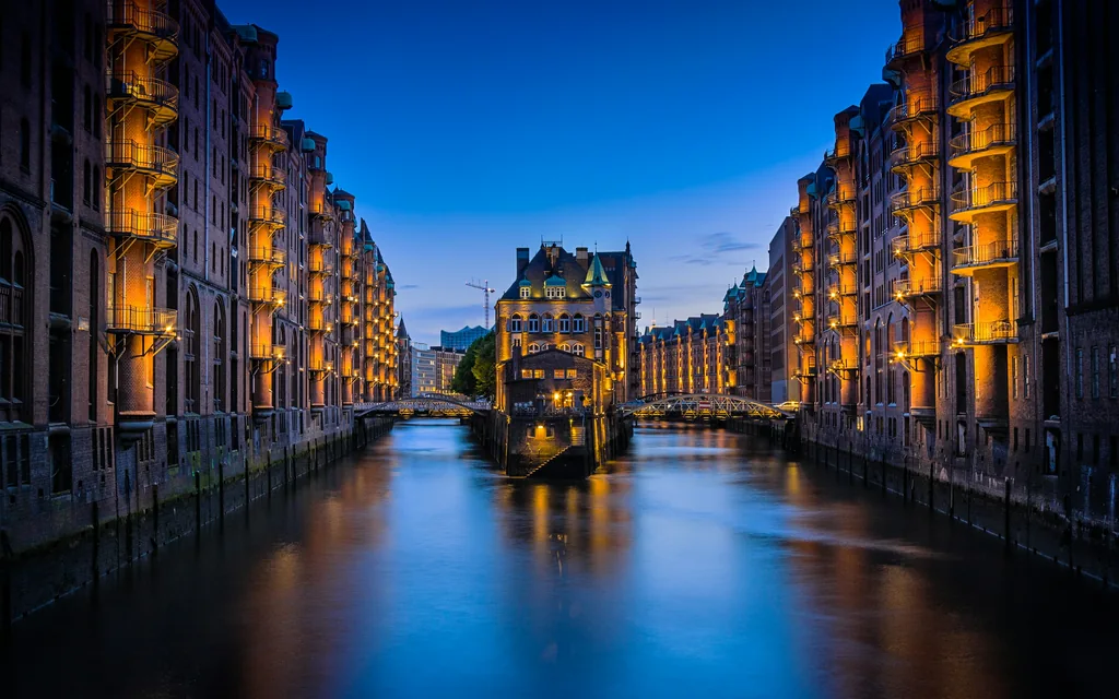 Beleuchtete Backsteinfassaden spiegeln sich zur blauen Stunde im Wasser der Speicherstadt